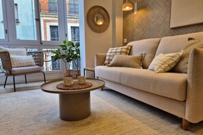 A living room with a beige sofa, a round coffee table, and a wicker chair. - 649A El rincon de Cimadevilla (Oviedo)