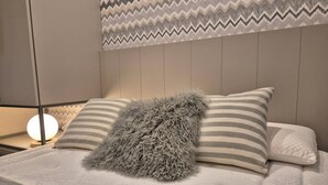 A bedroom with a bed, pillows, a fluffy throw, a bedside lamp, and a wall with a zigzag pattern.