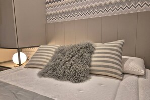 Un dormitorio con cama, almohadas, un plaid suave, una lámpara de noche y una pared con diseño en zigzag.