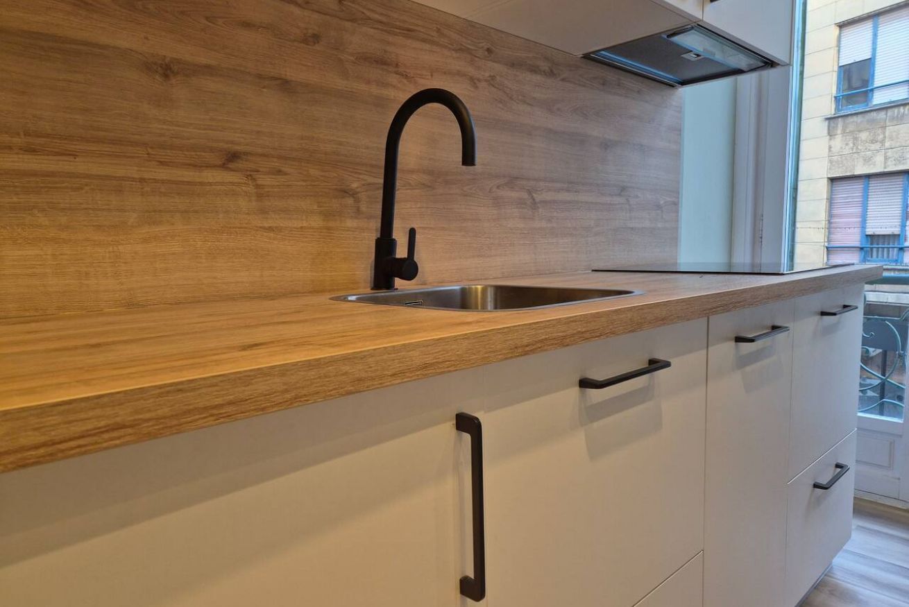 Een moderne keuken met een houten aanrecht, een zwarte kraan en witte kasten.