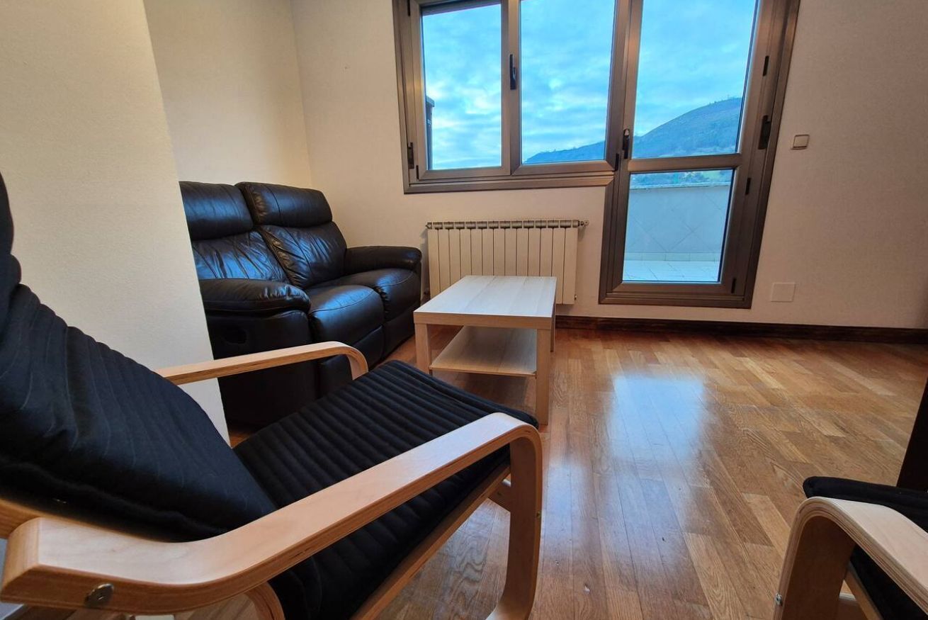 Una habitación con un sofá de cuero negro, una silla de madera, una mesita y una ventana con vistas al paisaje.