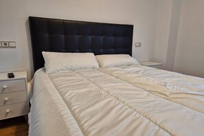 A neatly made bed with a black headboard, white bedding, and a bedside table with a remote control.
