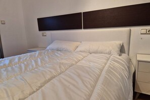 Een opgemaakt bed met witte lakens, een donker hoofdbord en een nachtkastje met een lamp.