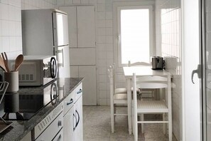 Ett kök med vita skåp, en mikrovågsugn, en spis och ett fönster.