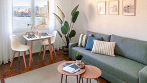 Uma sala de estar moderna com sofá, mesa de jantar, cadeiras, mesa de centro e uma planta grande.