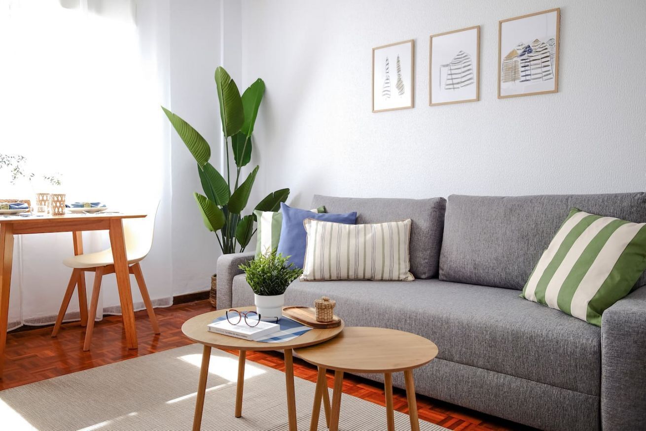 Een woonkamer met een grijze bank, een salontafel, een eettafel met stoelen en een potplant.