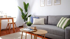 Ein Wohnzimmer mit grauem Sofa, einem Couchtisch, einem Esstisch mit Stühlen und einer Topfpflanze.