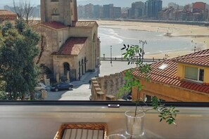 A view from a window overlooking a beach with a building that has a tower and arched windows.