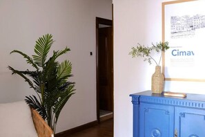 A hallway with a potted plant, a framed picture, and a blue cabinet.