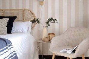 A bedroom with a bed, bedside table, chair, and a wall with vertical stripes.