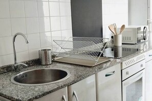 A kitchen with a granite countertop, stainless steel sink, and a microwave. - 130B Apartamento en Cimadevilla (Gijón)