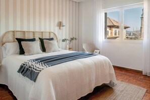 A bedroom with a large bed, a window with a view, and a small table with a plant. - 130B Apartamento en Cimadevilla (Gijón)