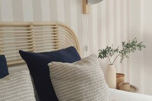 A bed with striped bedding, a wooden headboard, and a bedside plant.