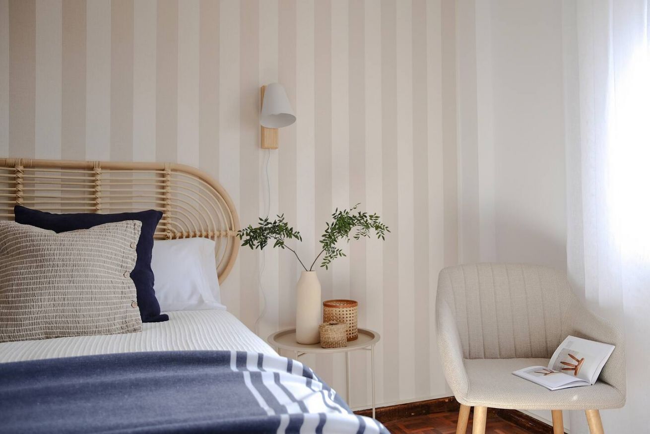Une chambre avec un papier peint à rayures, un lit avec une tête de lit, une table de chevet avec une lampe, une chaise et une plante.