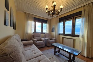 A living room with a sofa, two armchairs, a coffee table, a chandelier, and large windows with curtains.