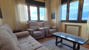 Un salon comprenant un canapé, deux fauteuils, une table basse et une vue sur le ciel par les fenêtres.