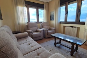 Un salon comprenant un canapé, deux fauteuils, une table basse et une vue sur le ciel par les fenêtres.