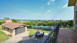 Un balcon donnant sur un paysage rural, un bâtiment en pierre avec un toit rouge et une table avec des chaises.