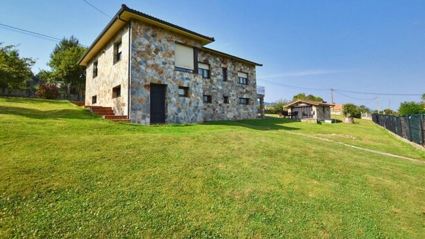 Un bâtiment en pierre de deux étages, doté d’un toit plat, d’une petite dépendance attenante et d’une cour gazonnée.