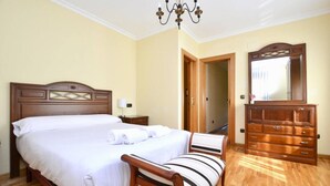 Une chambre à coucher avec un grand lit, une commode en bois, une chaise et un lustre.