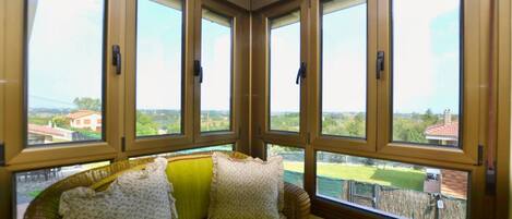 A room with a green sofa, four windows, and a view of a green landscape.
