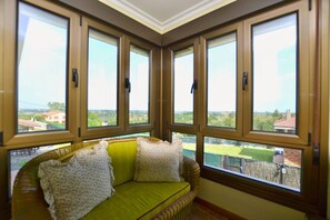 Una habitación con un sofá verde, cuatro ventanas y vistas a un paisaje verde.