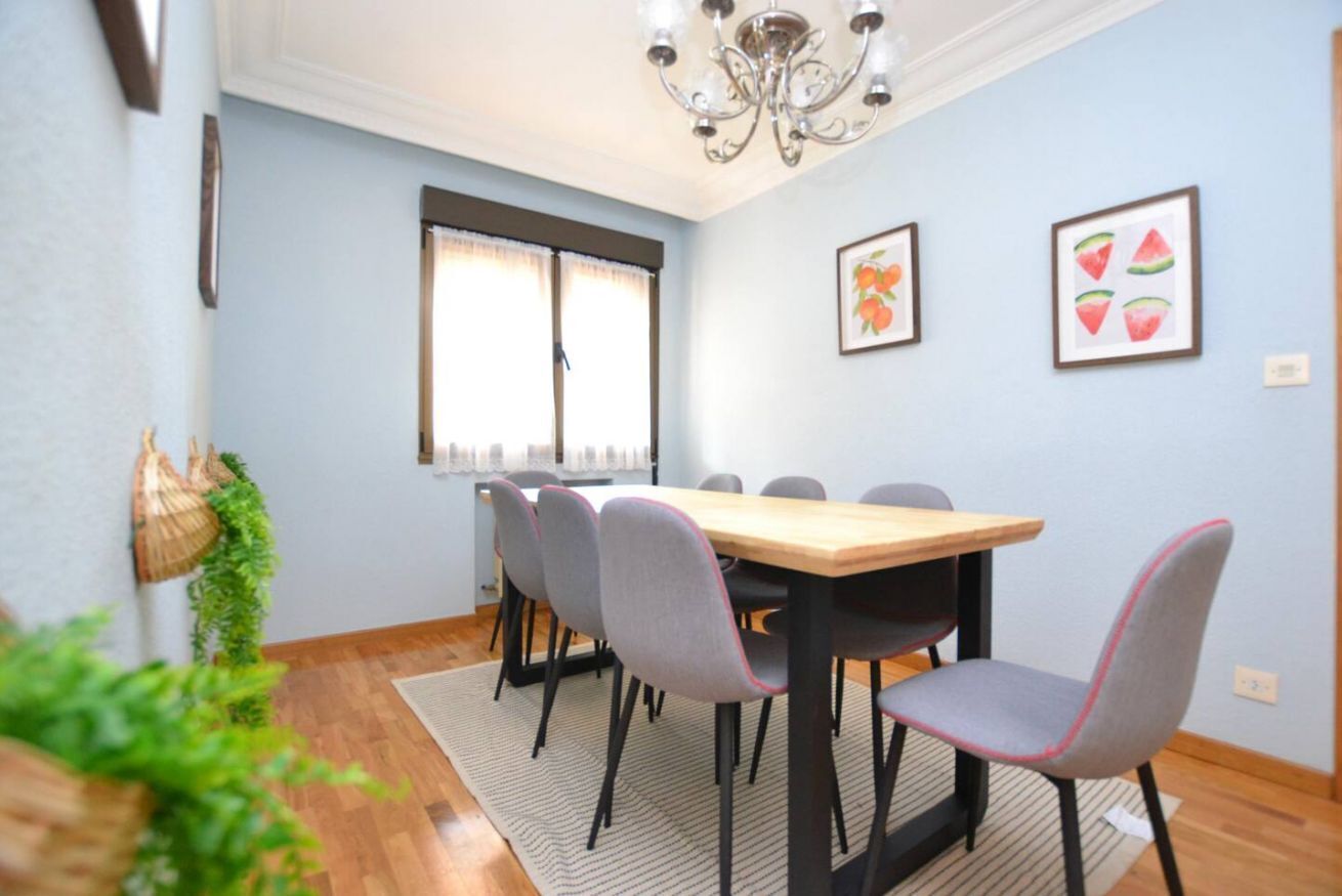 Un coin repas avec une table en bois, des chaises grises, un lustre et des œuvres d’art encadrées accrochées au mur.