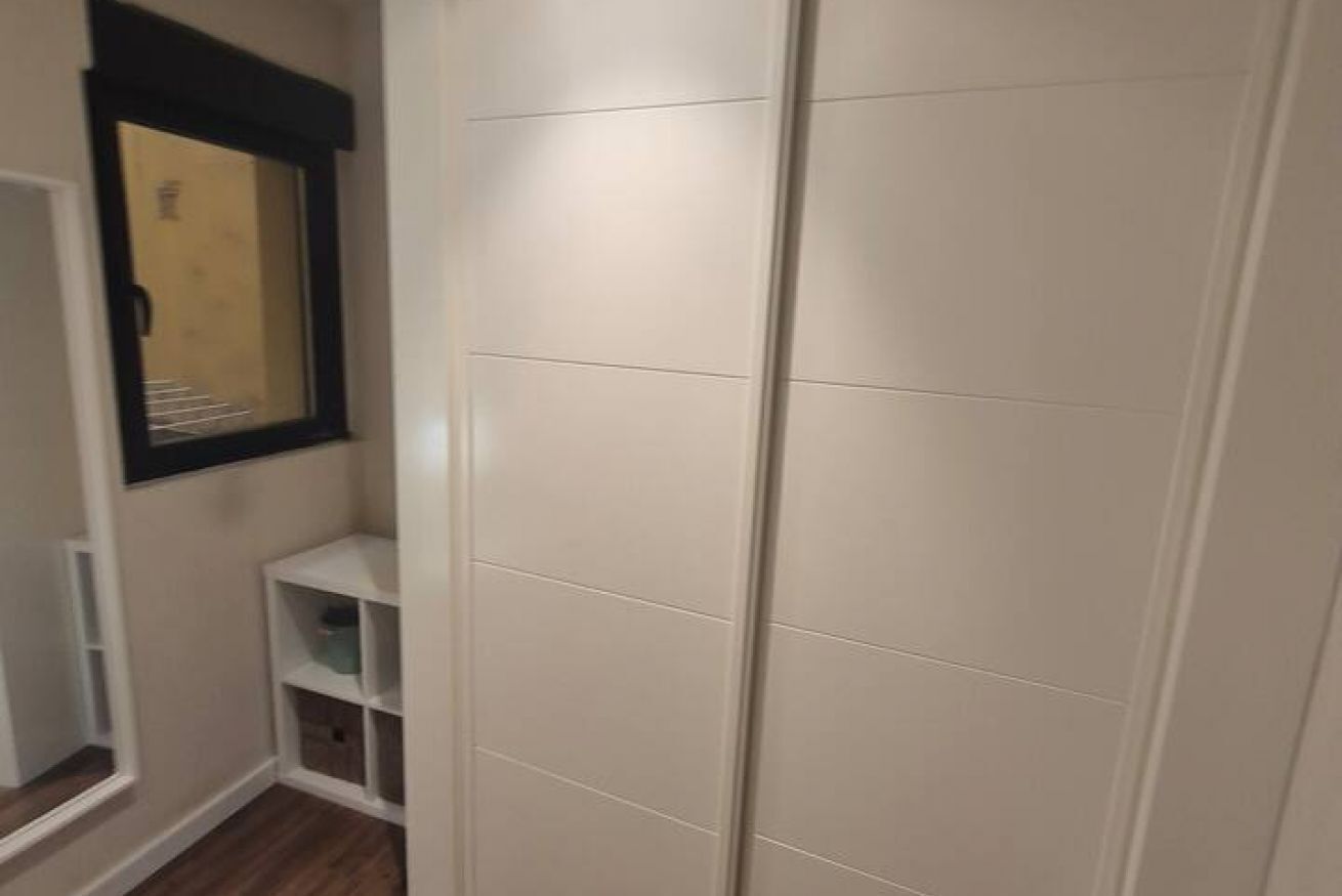 Een kamer met een kledingkast, een raam en een klein wandrek.