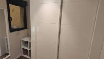 Een kamer met een kledingkast, een raam en een klein wandrek.