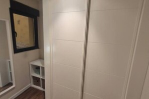 Quarto com guarda-roupa, janela e uma pequena estante.