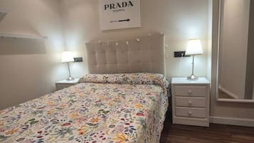 Een slaapkamer met een bloemenbed overtrek, een hoofdbord, twee nachtkastjes met lampen en een aan de muur bevestigd bord waarop 'PRADA MARFA' staat.