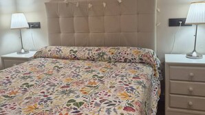 A bedroom with a floral bedspread, a tufted headboard, bedside lamps, and a nightstand. - 1A150 Apartamento céntrico en Gijón (Gijón)
