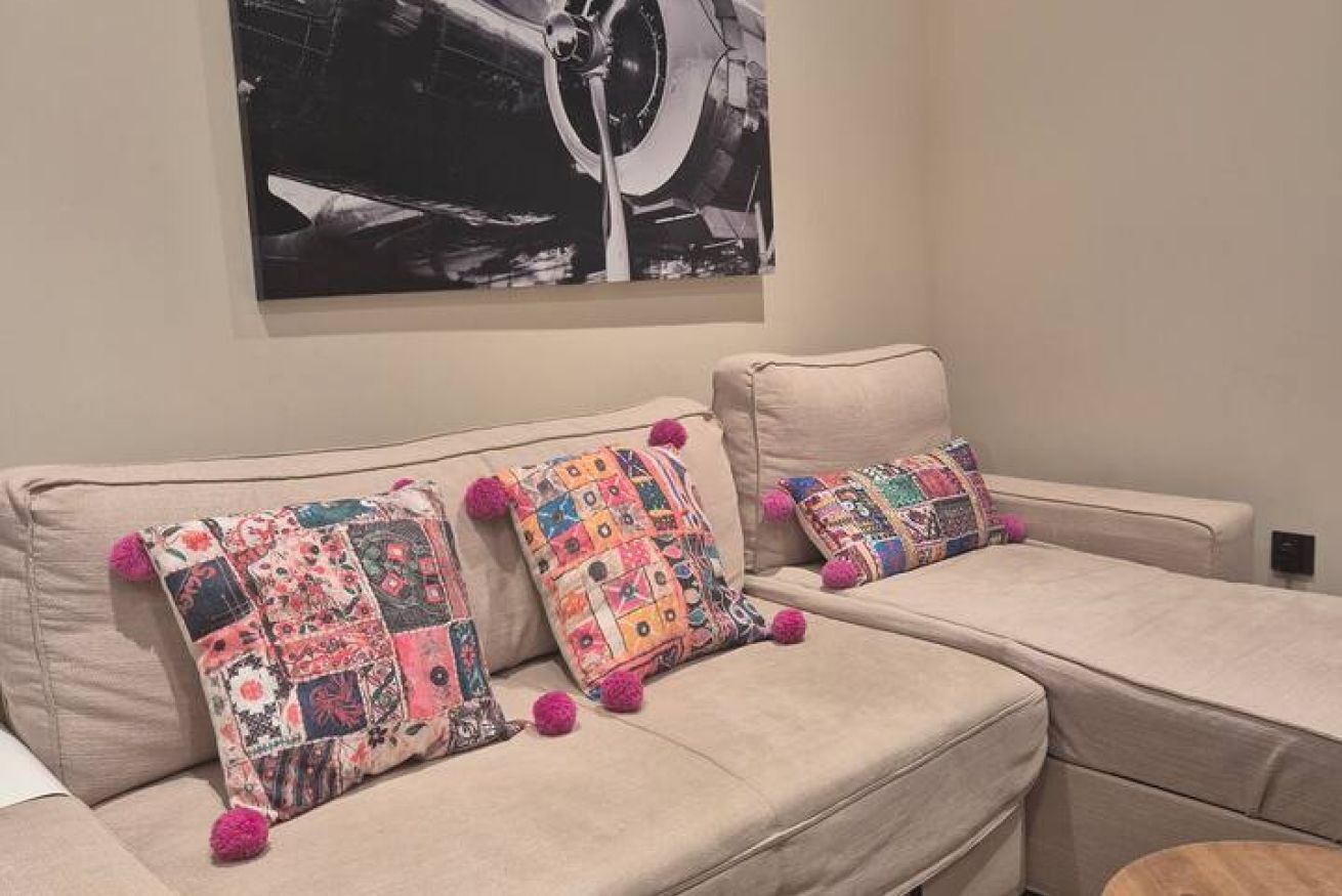 A beige sofa with colorful patchwork pillows and a black and white abstract painting above it.