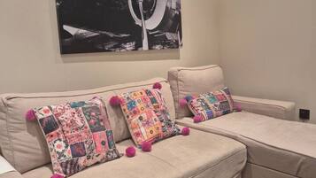 A beige sofa with colorful patchwork pillows and a black and white abstract painting above it.
