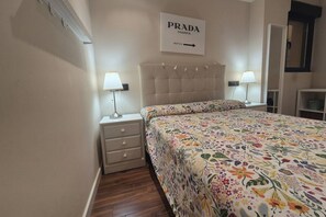 A bedroom with a floral bedspread, two bedside lamps, a nightstand with drawers, and a sign on the wall.