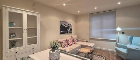 Ein modernes Wohnzimmer mit einem Glastisch, einer Sofagarnitur, einem Schrank und einem großen Fenster.