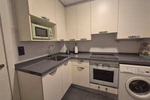 A compact kitchen with a microwave, sink, oven, and washing machine. - 1A150 Apartamento céntrico en Gijón (Gijón)