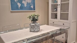 A dining table with a glass top, a white tablecloth, and a decorative vase with green plants. - 1A150 Apartamento céntrico en Gijón (Gijón)