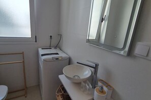 Ein Badezimmer mit weißem Waschbecken, einem Spiegel, einem Handtuchhalter und einer Toilette.