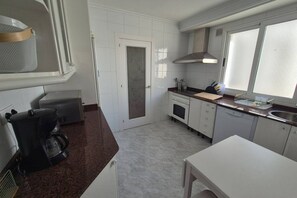Een kleine keuken met witte kastjes, een koffiezetapparaat, een fornuis en een raam met jaloezieën.