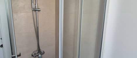 A shower with a handheld showerhead and a wall-mounted faucet.