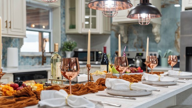 Un îlot de cuisine agrémenté d’un plateau de fruits, de bougies et de verres à vin en cuivre.