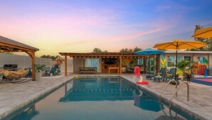 Un espace piscine avec des chaises longues, un barbecue et un coin salon abrité.