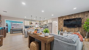 Une cuisine moderne avec des meubles en bois, un îlot central et un coin repas comprenant un canapé gris et un téléviseur fixé au mur.