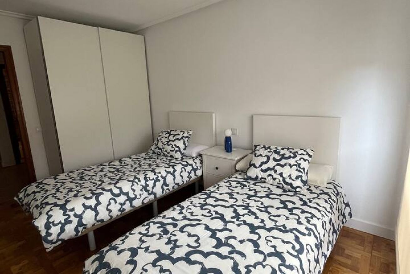 A room with two single beds, a nightstand, a wardrobe, and a white wall.
