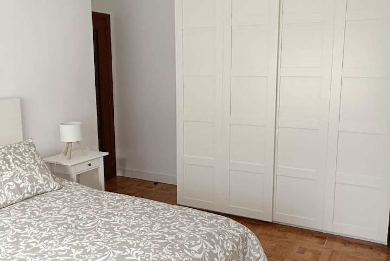 A bedroom with a bed, a nightstand, a lamp, and a wardrobe.