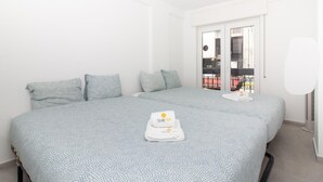 Een tweepersoonsbed met een beddegoed met patroon, twee kussens, een handdoek met een logo en uitzicht op een balkon met tuinmeubilair.