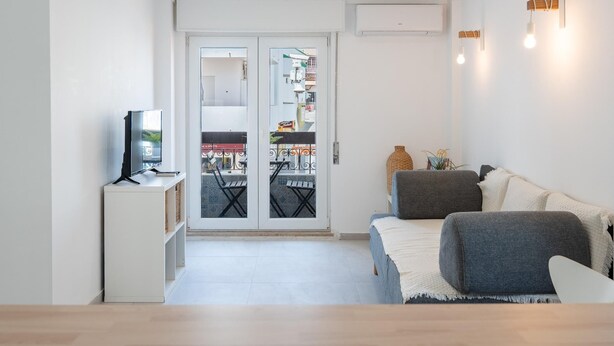 Een moderne woonkamer met een bank, een televisie en een balkon met uitzicht op de straat.