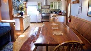 A wooden dining table with chairs, a kitchen with white cabinets, and a stone wall.