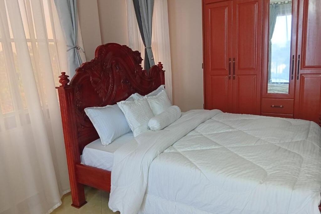 Una cama con cabecera de madera, ropa de cama blanca y un armario rojo al fondo.